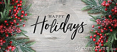 Happy Holidays Text with Holiday Evergreen Branches and Red Berries Frame Over Rustic Wooden Background Stock Photo