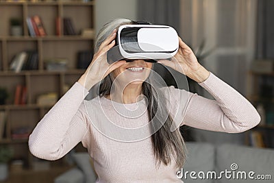 Happy inspired caucasian old lady with vr glasses enjoys leisure time, entertainment with device, wirtual world Stock Photo
