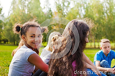 Happy international teens sit together on meadow Stock Photo