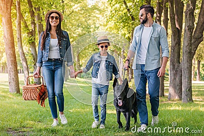 Happy interracial family with picnic basket walking with dog in forest Stock Photo