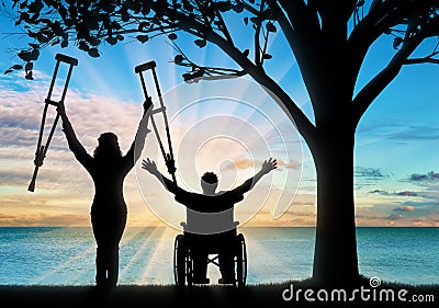 Happy invalids with crutches and in wheelchair near sea and tree Stock Photo