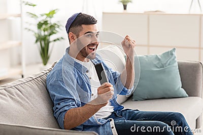 Happy jewish guy spending weekend watching tv shaking clenched fists Stock Photo