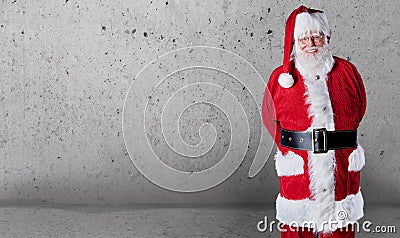 Happy jovial Santa Claus with copy space over a grey textured wall background to wish you a Merry Christmas Stock Photo