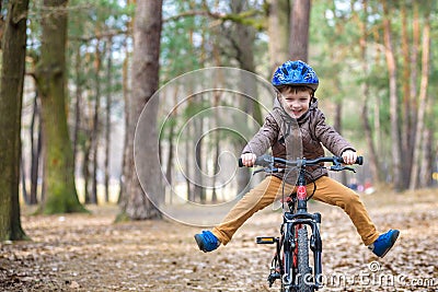 Happy kid boy of 3 or 5 years having fun in autumn forest with a bicycle on beautiful fall day. Active child wearing bike helmet. Stock Photo