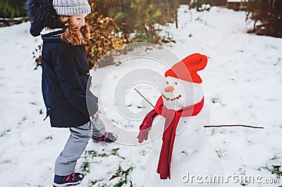 Happy kid girl making snow man on Christmas vacations on backyard Stock Photo