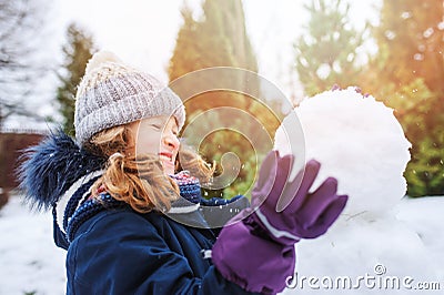 Happy kid girl making snow man on Christmas vacations on backyard Stock Photo