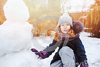 Happy kid girl making snow man on Christmas vacations on backyard Stock Photo