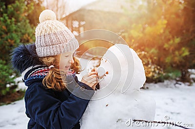 Happy kid girl making snow man on Christmas vacations on backyard Stock Photo