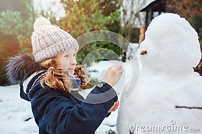 Happy kid girl making snow man on Christmas vacations on backyard Stock Photo