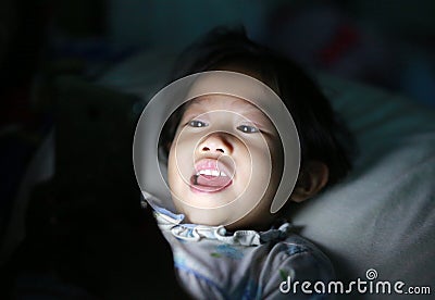 Happy Kid girl playing smartphone lying on a bed at night Stock Photo