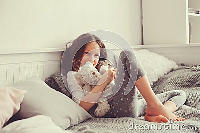 Happy kid girl playing with teddy bears in her room, sitting on bed Stock Photo