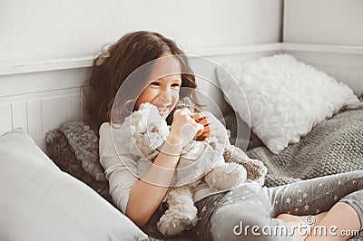 Happy kid girl playing with teddy bears in her room, sitting on bed Stock Photo