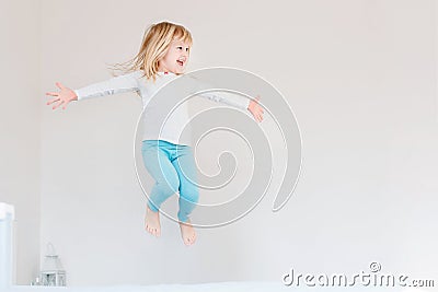 Happy kid jumping over bed. Cute little blond girl having fun indoors. Happy and careless childhood concept Stock Photo