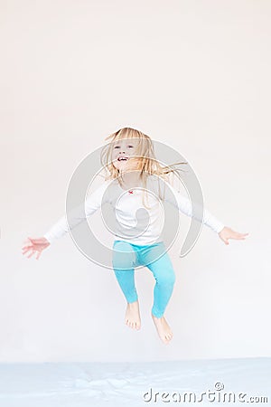 Happy kid jumping over bed. Cute little blond girl having fun indoors. Happy and careless childhood concept Stock Photo