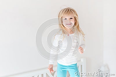 Happy kid jumping over bed. Cute little blond girl having fun indoors. Happy and careless childhood concept Stock Photo
