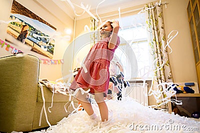 Happy kid on party, little girl having fun with confetti in playroom Stock Photo