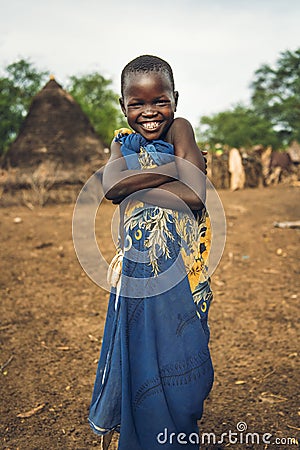 TOPOSA TRIBE, SOUTH SUDAN - MARCH 12, 2020: Happy kid wrapped in colorful cloth smiling for camera and crossing arms while living Editorial Stock Photo