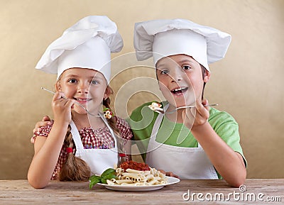 Happy kids with chef hats eating fresh pasta Stock Photo