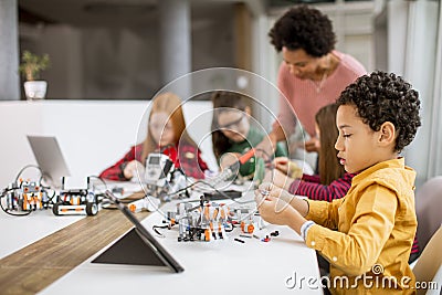 Happy kids with their African American female science teacher with laptop programming electric toys and robots at robotics Stock Photo