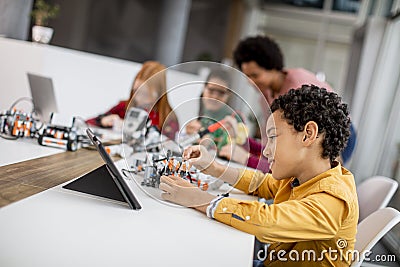 Happy kids with their African American female science teacher with laptop programming electric toys and robots at robotics Stock Photo