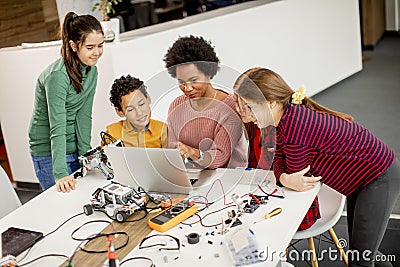 Happy kids with their African American female science teacher with laptop programming electric toys and robots at robotics Stock Photo