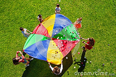 Happy kids waving rainbow parachute full of balls Stock Photo