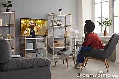 Happy woman sitting in chair in living-room and watching music video on television Stock Photo