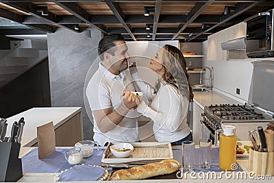 Happy latin couple eating yogurt with fruits while preparing breakfast in their kitchen Stock Photo