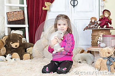 Happy laughing little girl playing with a baby rabbit, hugging her real bunny pet and learning to take care of an animal Stock Photo