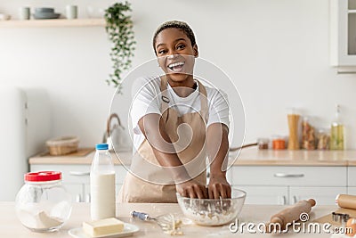 Happy laughing young black female in apron making dough, enjoy cooking pie in contemporary light kitchen Stock Photo