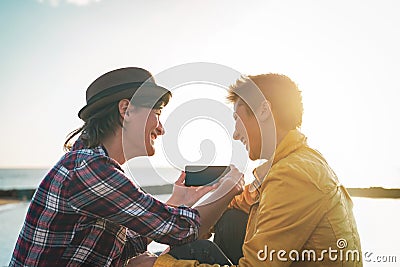 Happy lesbian couple watching on mobile phone next the beach at sunset - Young homosexual women having fun Stock Photo