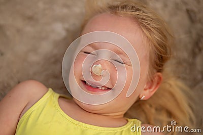 Happy littl girl lies on the sea sand with a seashell on her nose Stock Photo