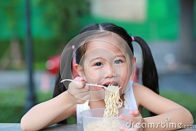 Happy little Asian child girl eating Instant noodles at the garden Stock Photo