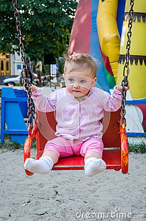 Happy little baby girl with a beautiful clasp on his head and jacket riding on a chain swing in amusement park Stock Photo