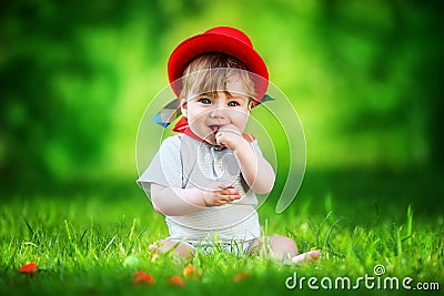 Happy little baby in red hat having fun in the park on solar glade. Summer vacations concept. The emotions. Stock Photo