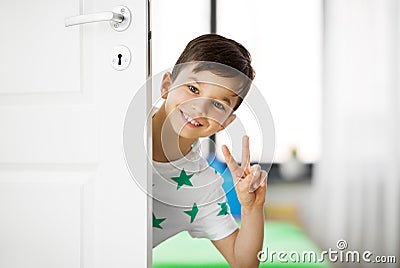 Happy little boy behind door at home showing peace Stock Photo