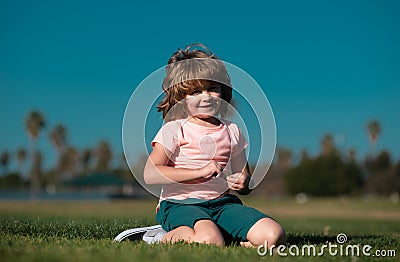 Happy little boy lying on the grass at the spring day. Portrait of a smiling child lying on green grass in park. Stock Photo