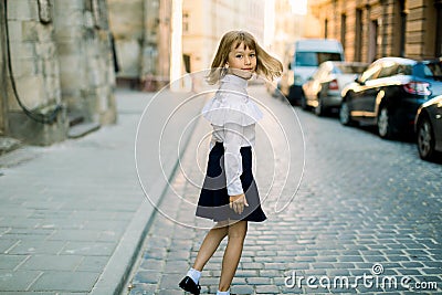 Happy little child, adorable blonde girl in black and white business wear, walking on old city street in ancient Stock Photo