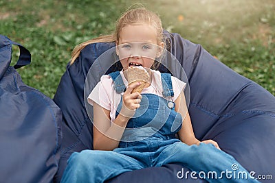 Happy little child, adorable toddler girl with blond hair and ponytail,wearing casual outfit, enjoying ice cream outdoors while Stock Photo