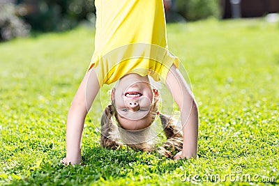 Happy little girl standing on her head on green lawn. Stock Photo