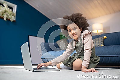 Happy little darkskinned girl with laptop sitting on floor Stock Photo