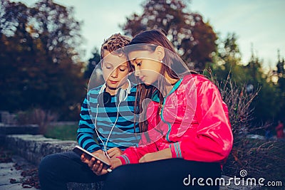 Happy little friends, boy and girl with headphones sharing music from a smart phone Stock Photo