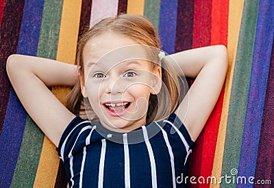 Happy little girl with crooked baby teeth in the colorful hammock summer background, summer holiday outdor activities Stock Photo