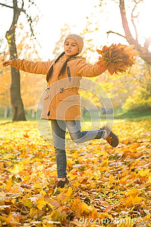 Happy little girl dancing on the fallen maple leaves in autumn park on cheerful fall day, vertica Stock Photo