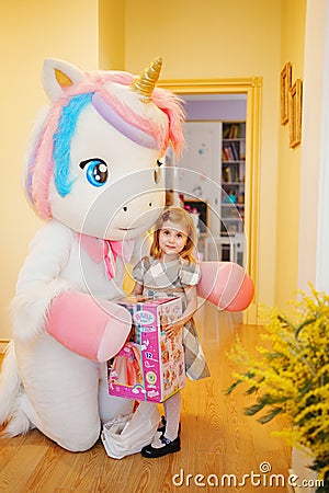 Happy little girl with a doll in a box and an animator in a unicorn costume. Editorial Stock Photo