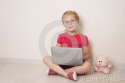Happy little girl in eyeglasses using notebook laptop sitting on the floor at home. Vision school education homeschooling e- Stock Photo