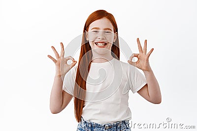 Happy little girl with ginger hair shows okay signs and smiles satisfied. Pleased young child with red head say yes Stock Photo
