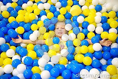 Happy little girl having fun in ball pit in kids indoor play center. Child playing with colorful balls in playground ball pool. Stock Photo
