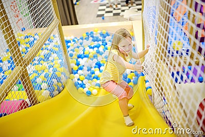 Happy little girl having fun in ball pit in kids indoor play center. Child playing with colorful balls in playground ball pool. Stock Photo