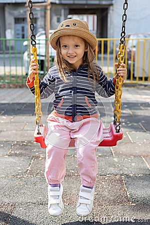 Happy little girl having fun on outdoor playground. Swinging on swing Stock Photo